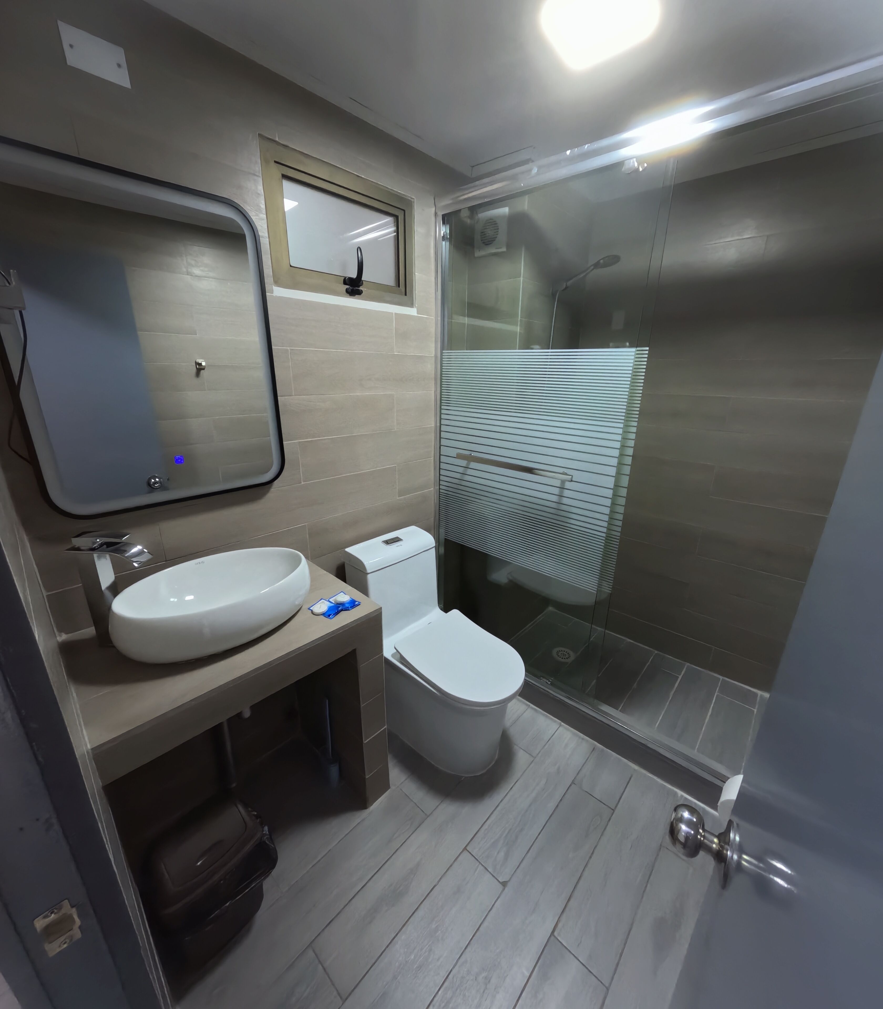 Un baño moderno con un espejo grande, un lavamanos, un inodoro y una zona de ducha con mampara de vidrio.