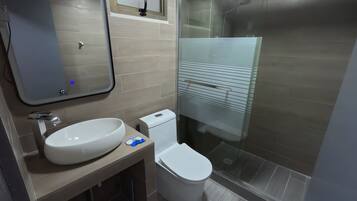 Un baño moderno con un espejo grande, un lavamanos, un inodoro y una zona de ducha con mampara de vidrio.