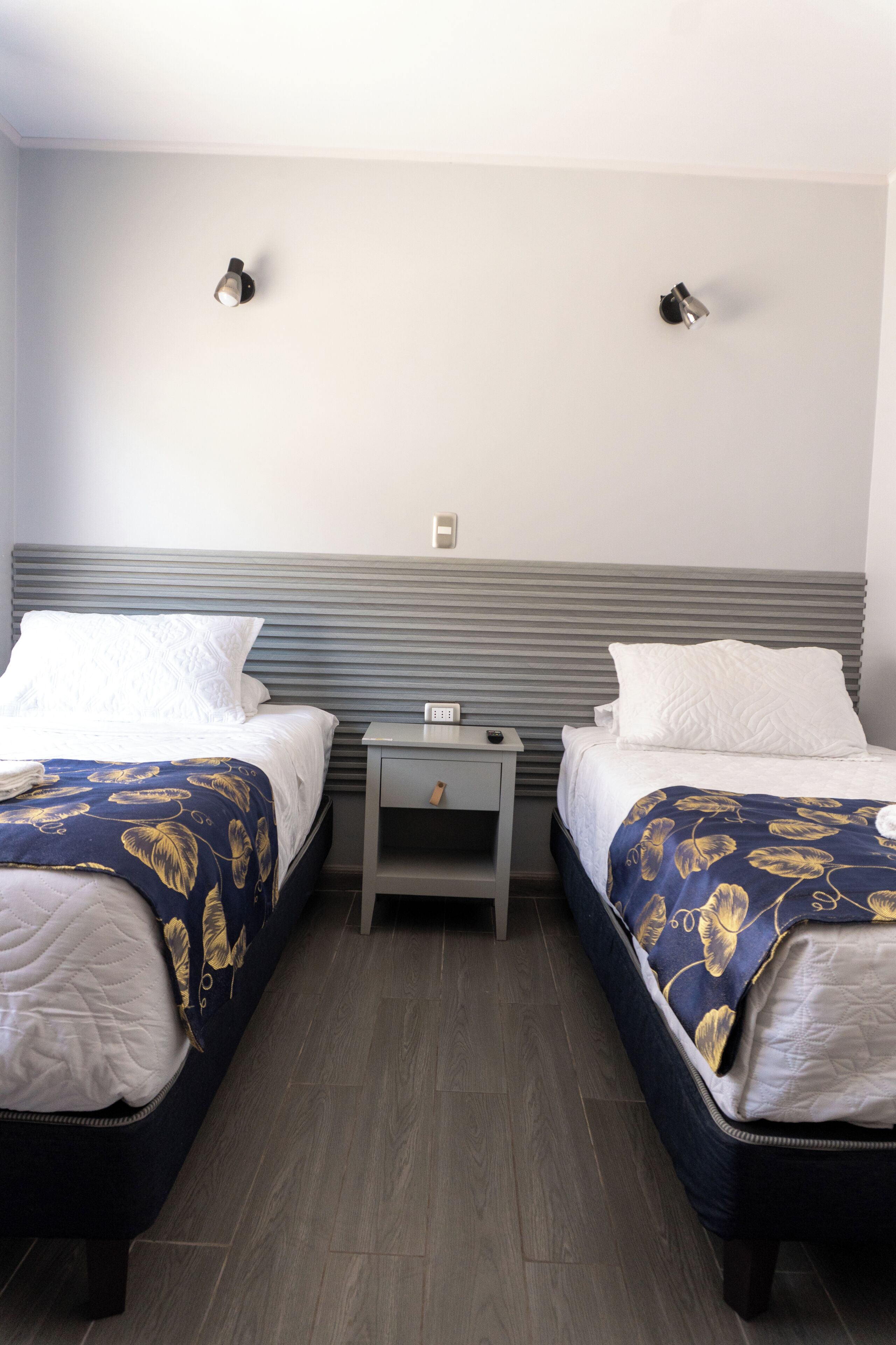 Habitación de hotel con dos camas, una mesita de noche e iluminación en la pared.