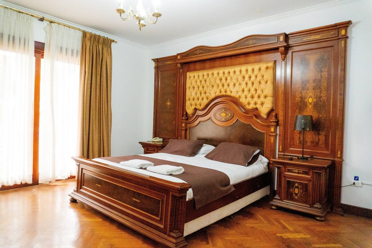 A bedroom with a large bed, wooden headboard, bedside tables, and a chandelier.