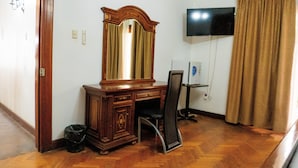 A room with a wooden desk, a chair, a large mirror, a television on the wall, and a curtain. - Hotel Divasto (Iquique)
