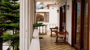 A balcony with a tiled floor, wooden chairs, a potted plant, and a view of a building in the background. - Hotel Divasto (Iquique)
