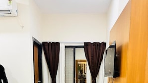 Une chambre d’hôtel avec un lit, une table de chevet en bois, un miroir, un téléviseur fixé au mur et une porte-fenêtre coulissante avec des rideaux.