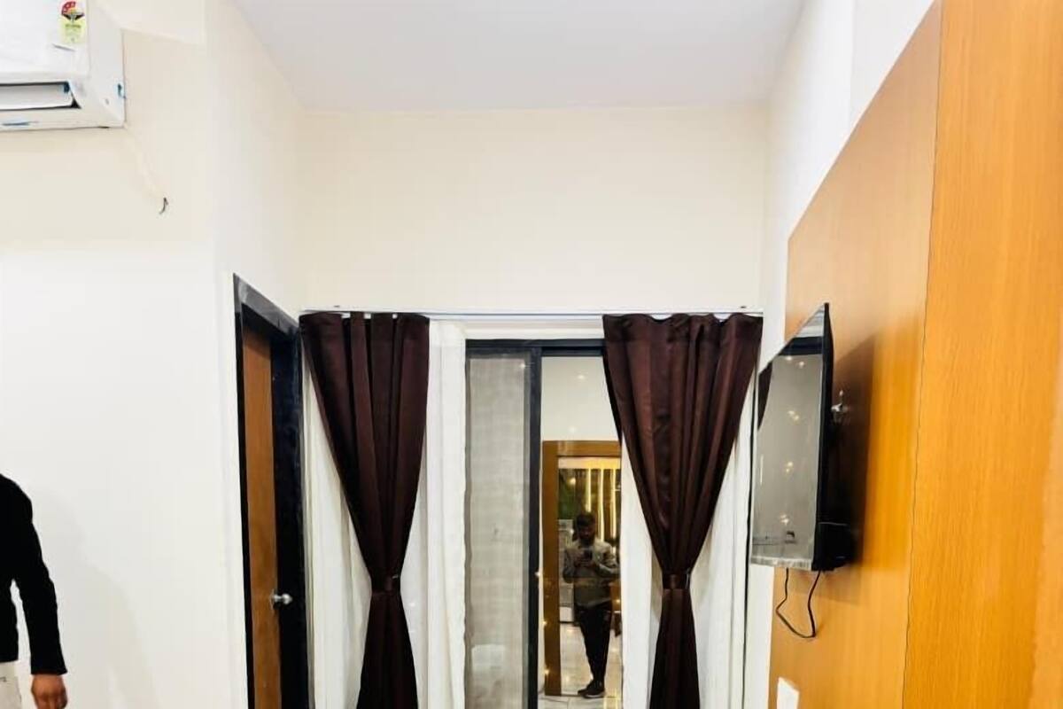 Une chambre d’hôtel avec un lit, une table de chevet en bois, un miroir, un téléviseur fixé au mur et une porte-fenêtre coulissante avec des rideaux.