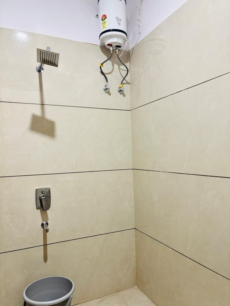 A corner bathroom with a shower, a toilet, and a bucket.