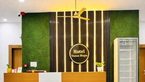 Un comptoir d’accueil d’hôtel agrémenté d’un mur végétal, d’une bande lumineuse verticale et d’un ventilateur de plafond.