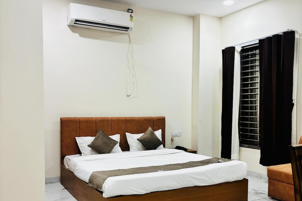 Une chambre bien rangée, avec un lit, un ventilateur de plafond, un appareil de climatisation et une fenêtre avec des rideaux.