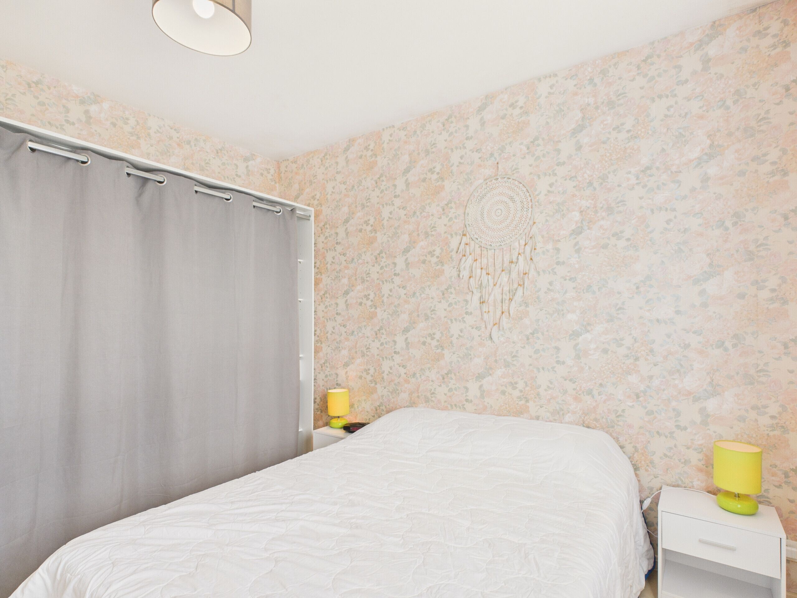Un dormitorio con una cama, una mesita de noche, una lámpara y un atrapasueños en la pared.