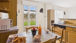 Une cuisine équipée d’une table à manger, de chaises, d’un réfrigérateur, d’un évier et d’une fenêtre donnant sur l’extérieur.