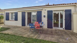Un bâtiment à deux étages doté d’un patio comprenant une table et des chaises, une porte-fenêtre coulissante et un petit jardin.