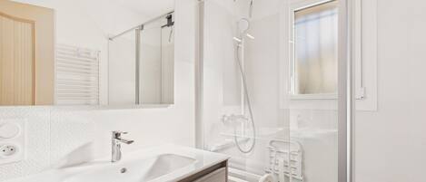 Un baño moderno con ducha de vidrio, un espejo grande y un lavabo blanco.