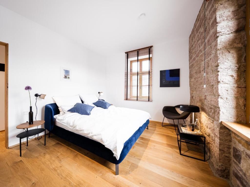 Une chambre moderne avec un grand lit, une petite table, une chaise et un mur en pierre.