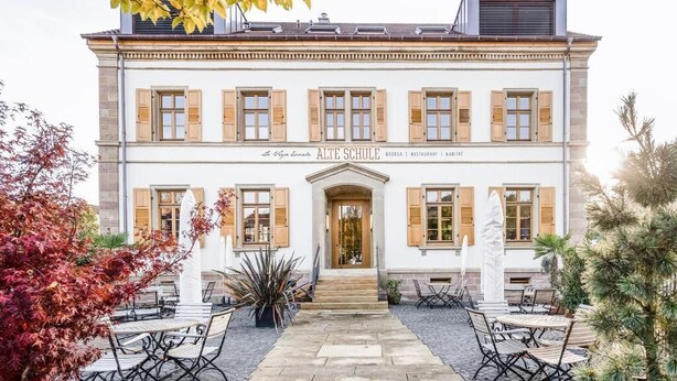 A two-story building with a central entrance, outdoor seating area, and a sign indicating it is a restaurant, hotel, and restaurant. - Alte Schule Tiefenbach  (Östringen)