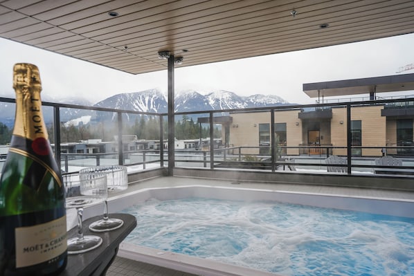 Un bain à remous avec vue sur les montagnes, une bouteille de champagne et un verre sur un balcon.