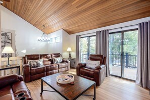 Ein geräumiges Wohnzimmer mit Holzboden, Ledersofas, einem Couchtisch und großen Fenstern mit Blick ins Freie.