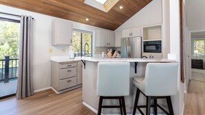 A modern kitchen with white cabinets, a stainless steel refrigerator, and a large island with bar stools. - ROCK06 - Luxurious Sunriver Home, Hot Tub (Sunriver)
