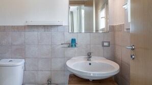 Un baño con lavamanos blanco, un espejo, inodoro y zona de ducha.