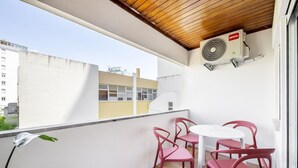 A balcony with a white table and four red chairs, an air conditioning unit, and a view of buildings in the background. - Amarelo Studio by Olala Homes  (Cascais)