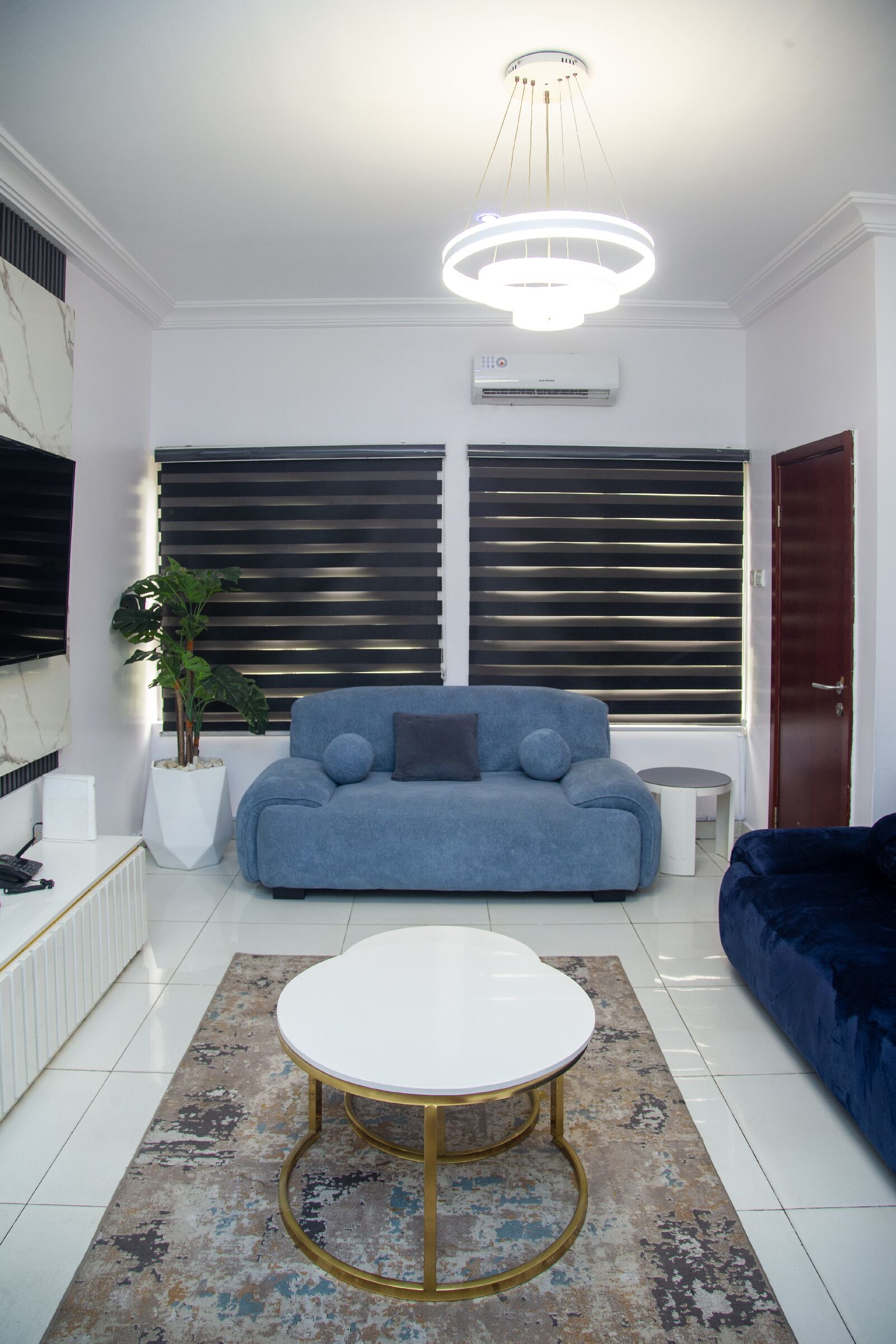 A modern living room with a blue sofa, a white coffee table, and a potted plant.