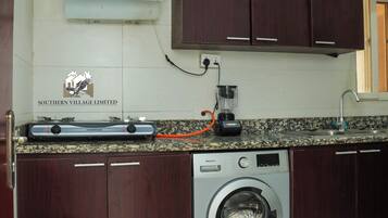 A kitchen with dark wooden cabinets, a built-in washing machine, a countertop with a blender, and a sign for Southern Village Limited.