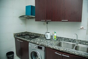 A compact kitchen with a built-in washing machine, a gas stove, and a double sink. - Southern Village Serviced Apartments (Lekki)
