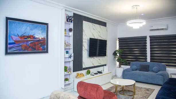 Una sala moderna con un televisor grande, un sofá rojo, un sofá azul y una pared de acento de mármol.