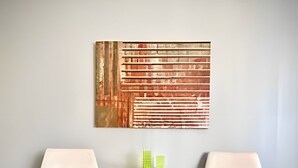 A room with two white chairs, a small round table with a green object on it, and a large abstract painting on the wall. - Residencial Liberdade (São Paulo)