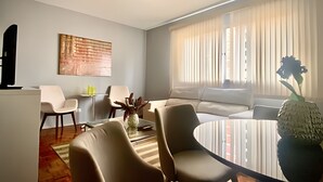 A modern living room with a round coffee table, two armchairs, a sofa, a ceiling fan, and a large window with blinds. - Residencial Liberdade (São Paulo)