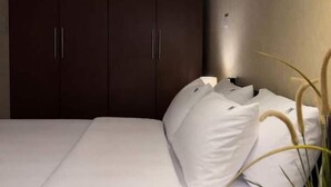 A bedroom with a bed, white pillows, and dark wooden wardrobe. - Wanderlust Awaits – Your Stylish Retreat in Maadi (Cairo)