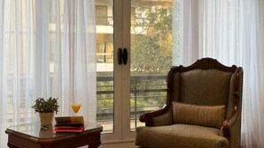 A room with a large sliding glass door leading to a balcony, a wooden chair, a small table with a plant and a glass of orange juice, and a book. - Wanderlust Awaits – Your Stylish Retreat in Maadi (Cairo)