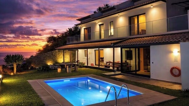 Een twee verdiepingen tellend huis met een zwembad, buiten zitplaatsen en uitzicht op de zonsondergang.