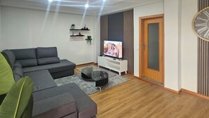 Een moderne woonkamer met een modulaire bank, een flatscreen televisie, een houten deur en een wandklok.