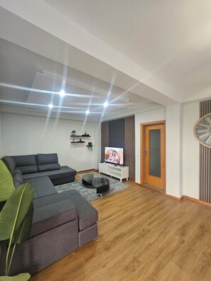 A modern living room with a sectional sofa, a flat-screen TV, a wooden door, and a wall clock. - Villa Barros (Câmara de Lobos)
