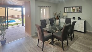 Een eetruimte met een glazen tafel, vier stoelen, een vaas met bloemen en uitzicht op een zwembad.