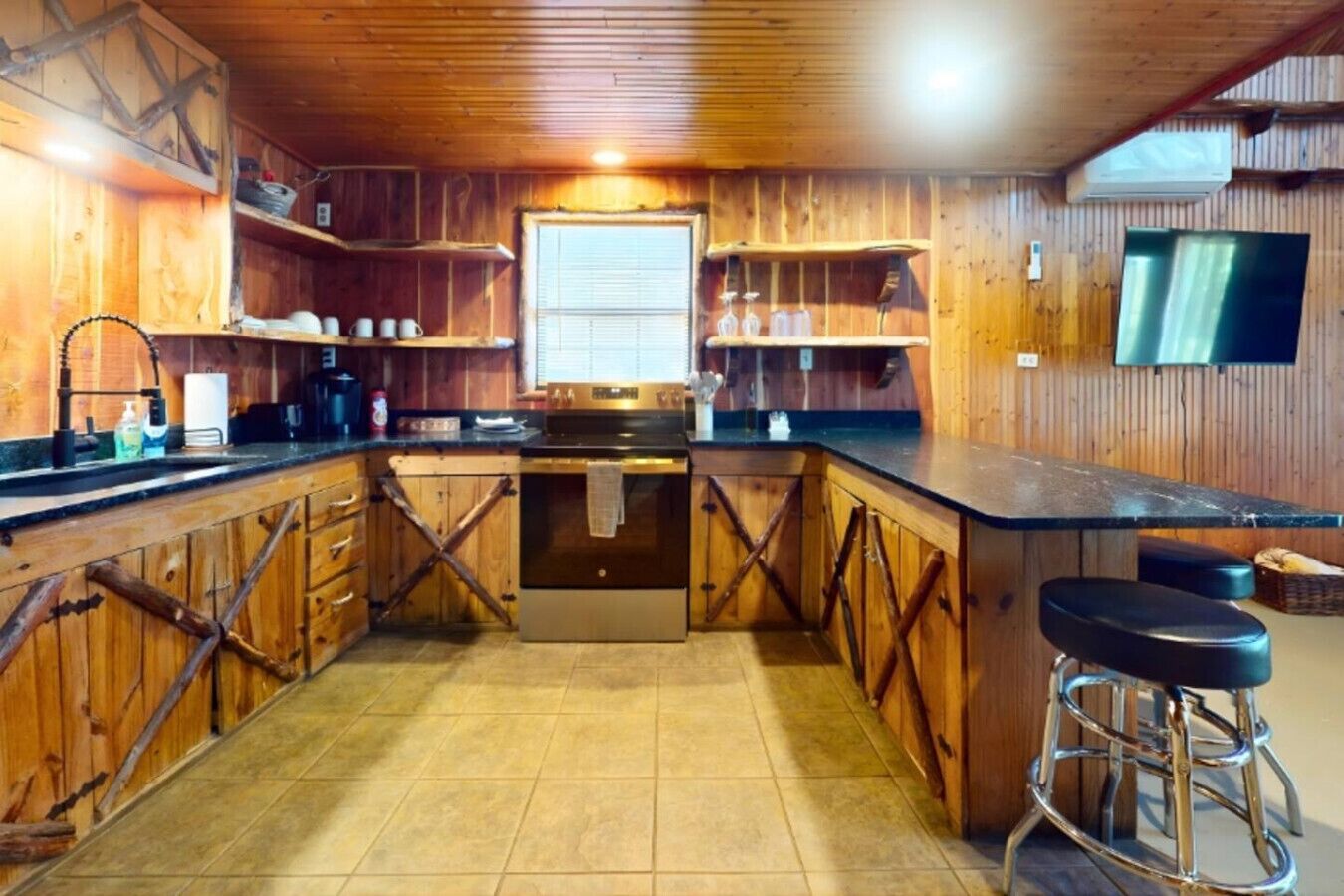 Een keuken met houten kastjes, een centraal eiland, barstoelen en een televisie aan de muur.