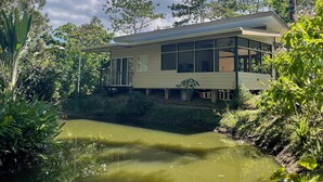 A modern house with large windows, a balcony, and a pond in the foreground.