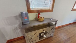 Une console en bois dotée d’un meuble à vin intégré, d’une machine à café Keurig et d’un panier contenant du pain.