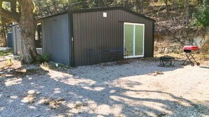 Un petit abri en métal, de plain-pied, doté d’une porte coulissante en verre, d’un banc et d’un barbecue à l’extérieur.