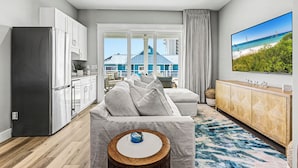 A modern kitchen with a stainless steel refrigerator, a dining area with a white table and chairs, and a large window offering a view of a blue building and beach. - Private Pool Rooftop Deck w/ Panoramic Views It's A Shore Thang (Navarre)