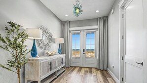 A hallway with a wooden floor, a potted plant, a console table with lamps, a mirror, and a view through a door to the outside. - Private Pool Rooftop Deck w/ Panoramic Views It's A Shore Thang (Navarre)
