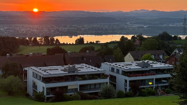 Un edificio moderno con techo plano, varios balcones y vistas a un lago al atardecer.