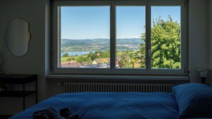 Un dormitorio con un ventanal grande, una cama, un radiador y un espejo fijado a la pared.