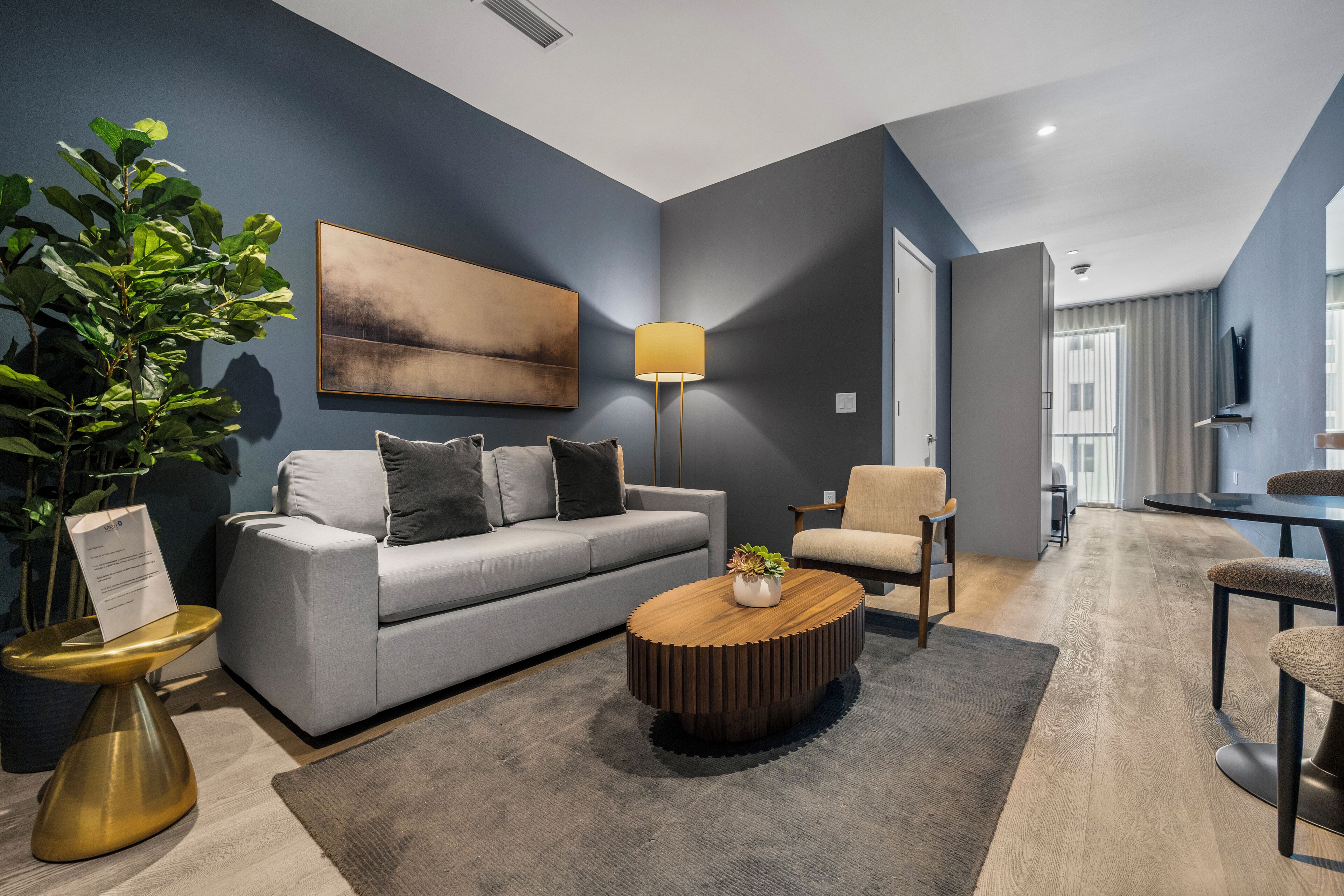 A modern living room with a grey sofa, a wooden coffee table, a floor lamp, and a large potted plant.