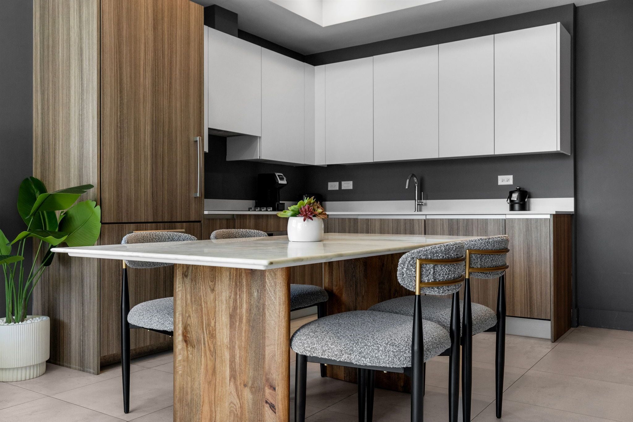 A modern kitchen with white cabinets, a wooden accent wall, and a dining area with a marble table and upholstered chairs.