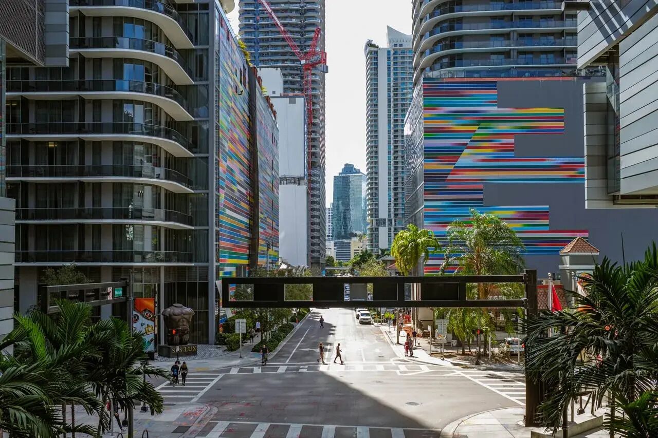 Une rue moderne en milieu urbain, bordée d’immeubles de grande hauteur, avec un passage piéton et des palmiers.