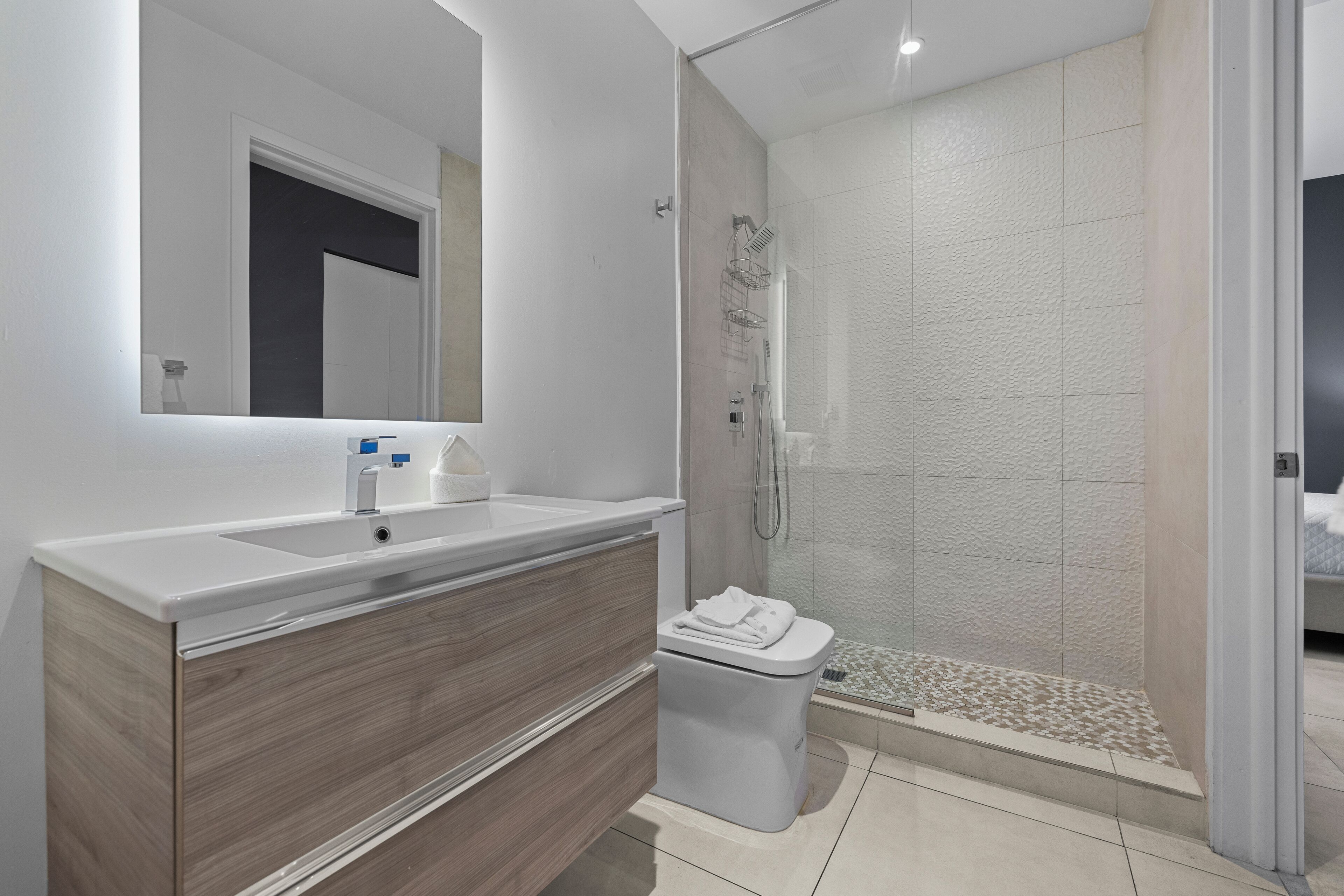 Une salle de bain moderne avec un grand miroir, un lavabo, des toilettes et une douche séparée par une paroi en verre.