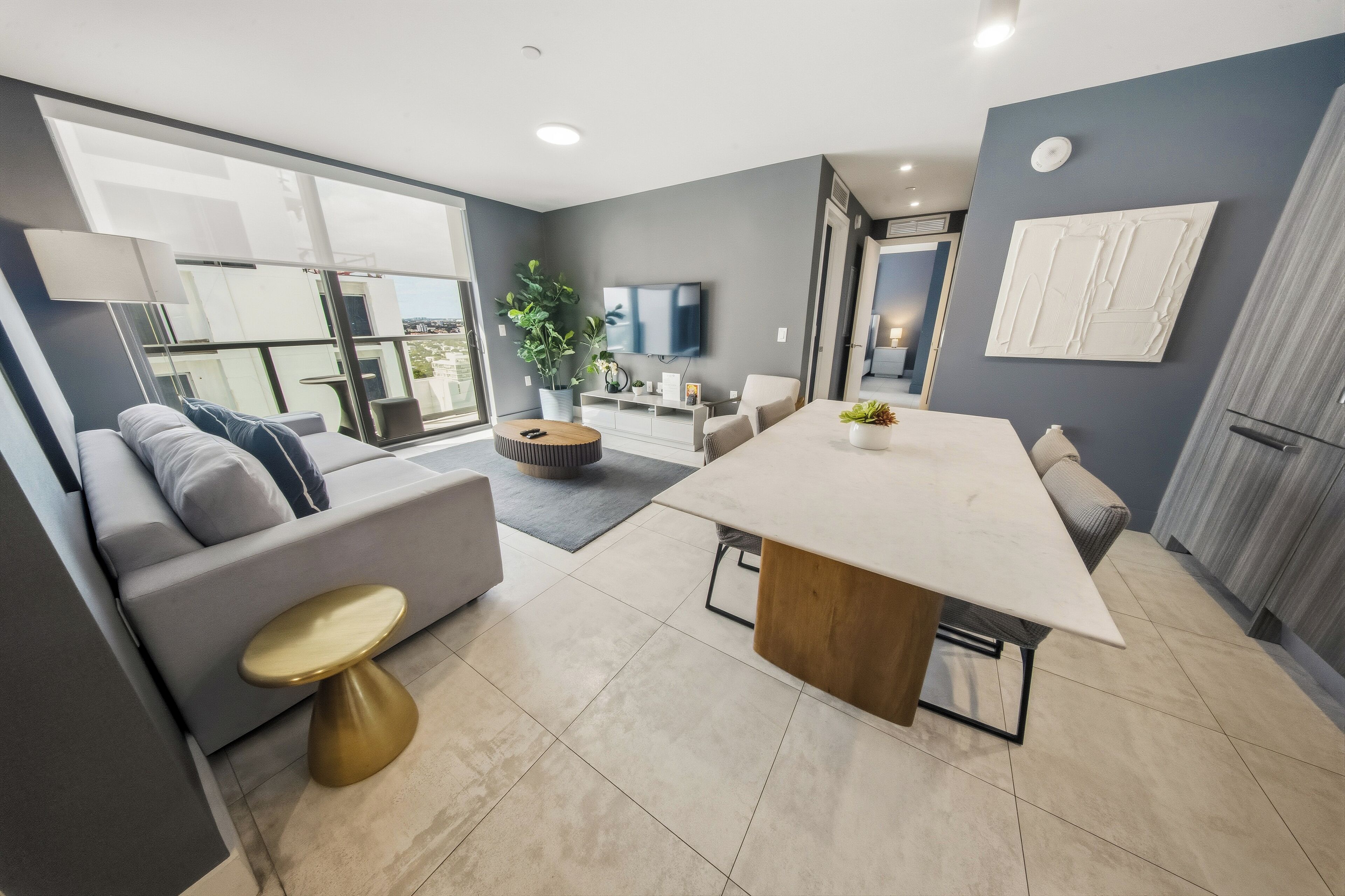 Una sala de estar moderna con un sofá gris, una mesa de centro, una mesa de comedor y un televisor montado en la pared.