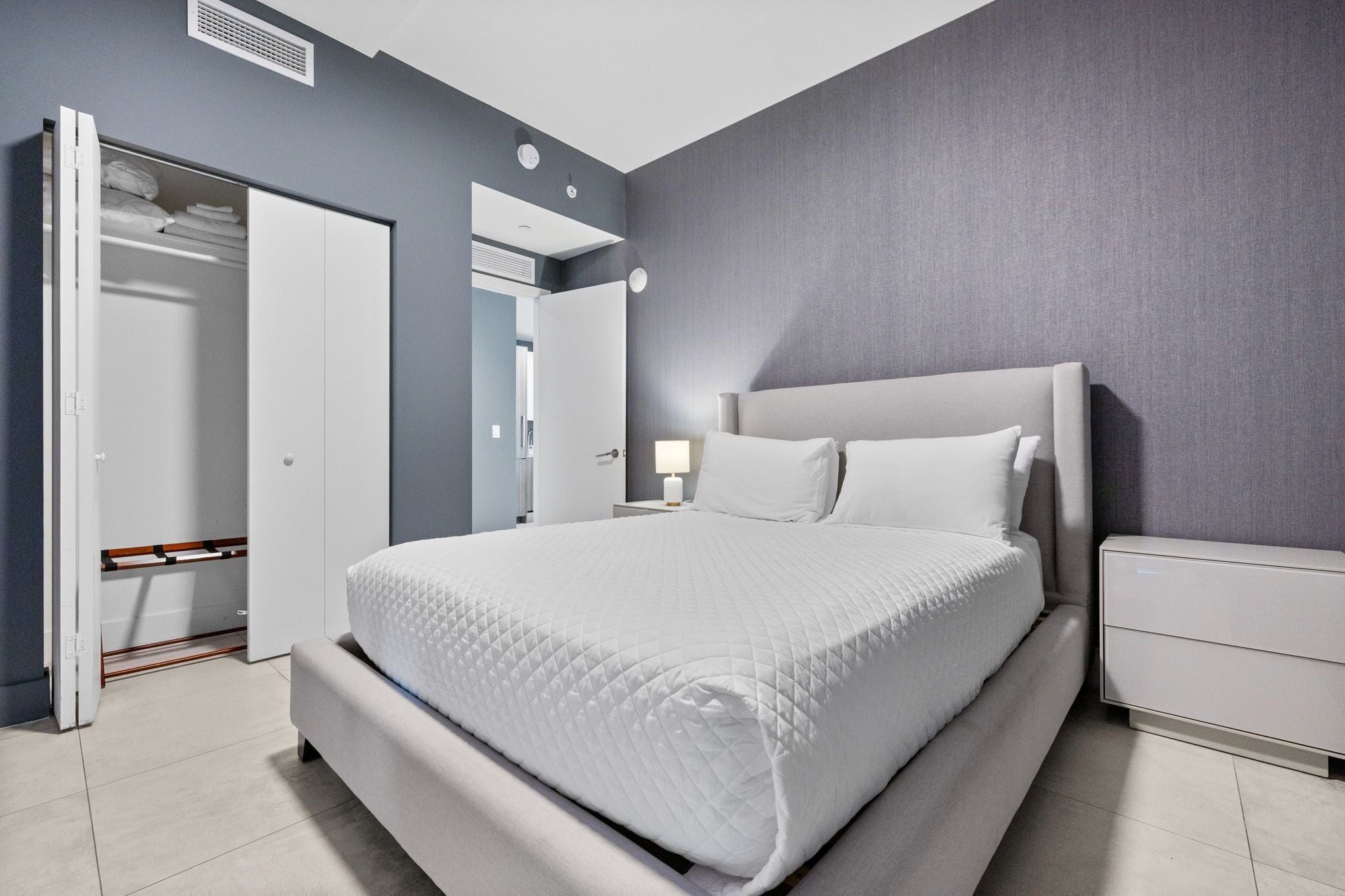 A modern bedroom with a large bed, a bedside table, a wardrobe, and a nightstand.