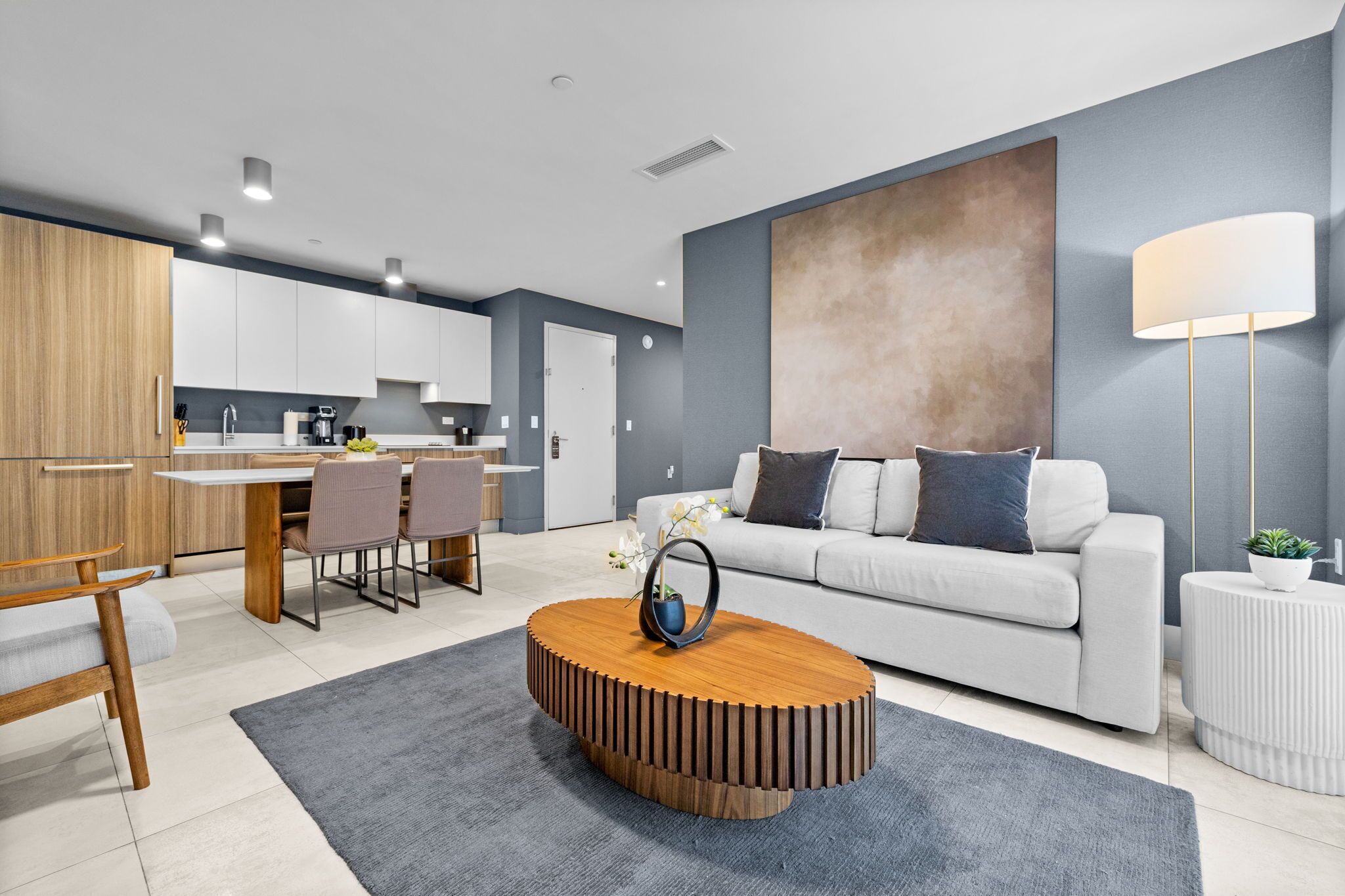 A modern living room with a round wooden coffee table, a grey rug, a white sofa, and a large abstract painting on the wall.
