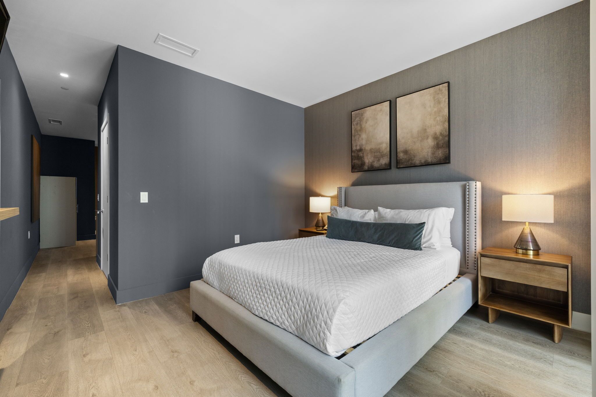 Un dormitorio moderno con una cama grande, lámparas de noche y vistas a un pasillo.